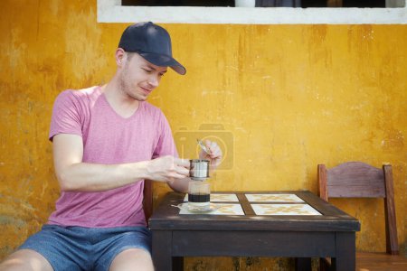 Téléchargez les photos : Homme dégustant un verre de café vietnamien chaud traditionnel avec du lait condensé. Voyageur au Vietnam. - en image libre de droit