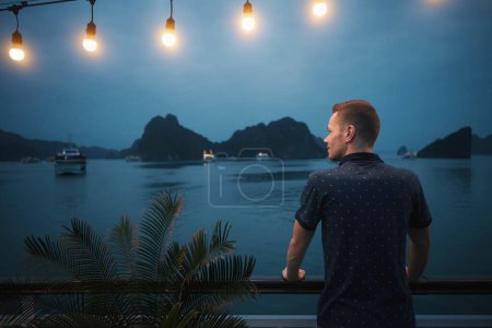 Foto de Hombre disfrutando de una magnífica vista nocturna desde un crucero entre islas. Destino turístico popular con formaciones kársticas en el mar, Ha Long Bay en Vietnam - Imagen libre de derechos