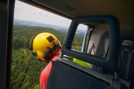 Photo for Rescue in difficult to access terrain. Paramedic of Helicopter Emergency Medical Service looking down from open door of  helicopter - Royalty Free Image
