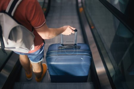 Reisende gehen durch das Flughafenterminal. Rückansicht eines Mannes mit Koffer und Rucksack, der auf einem Kühlschrank steht. Passagier ist reif für die Reise