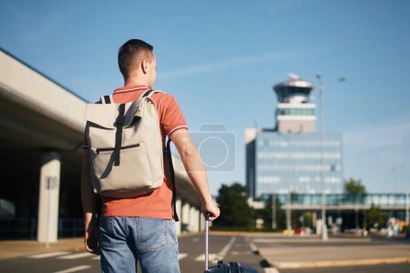 Foto de Viajar en avión. El viajero está caminando a la terminal del aeropuerto. Hombre con maleta contra torre de control de tráfico aéreo. - Imagen libre de derechos