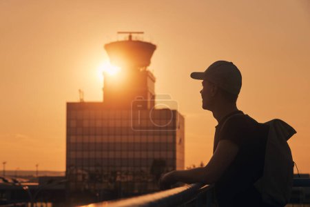 Photo for Traveler with backpack at airport. Silhouette of man against air traffic control tower at sunset - Royalty Free Image