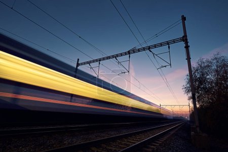 Foto de Ferrocarril al amanecer. Larga exposición del tren en la vía férrea. Tren de pasajeros interurbano moderno en movimiento - Imagen libre de derechos