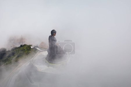 Téléchargez les photos : Statue de Bouddha en bronze au sommet du sommet de la montagne Fansipan dans un brouillard mystérieux. Province de Lao Cai, Viêt Nam - en image libre de droit