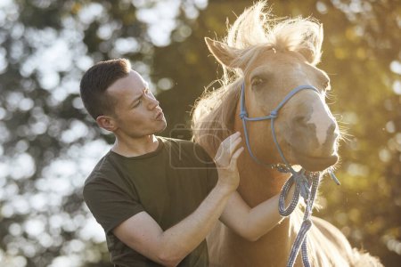 Foto de Retrato del hombre calmando caballo durante el entrenamiento de obediencia en el soleado día de verano - Imagen libre de derechos