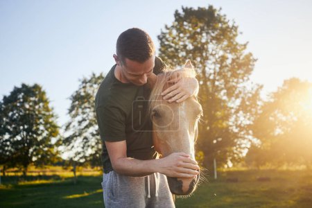 Foto de El hombre está abrazando al caballo de terapia en el prado al atardecer. Temas hipoterapia, cuidado y amistad entre personas y animales - Imagen libre de derechos