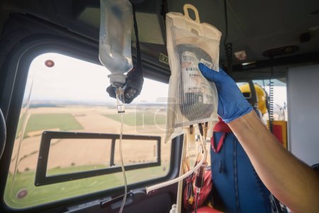 Foto de Mano del médico que sostiene la bolsa de transfusión con sangre a bordo del helicóptero del servicio médico de emergencia durante el vuelo al hospital. Temas de rescate, urgencia y atención sanitaria - Imagen libre de derechos