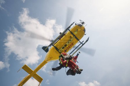 Photo for Two paramedics hanging on rope under flying helicopter emergency medical service. Themes rescue, help and heroes - Royalty Free Image