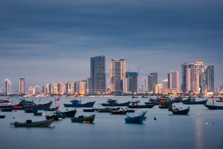 El paisaje urbano de Da Nang al atardecer. Barco pesquero amarrado en puerto contra costa iluminada con edificios modernos