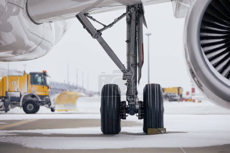 Photo for Winter day at airport during snowfall. Selective focus on snowy airplane. Snowplows clearing snow from runway - Royalty Free Image