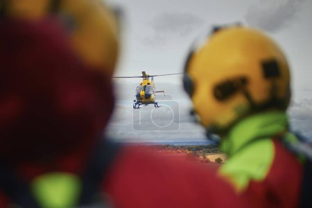 Rückansicht von Sanitätern mit Helmen beim Blick auf den herannahenden Hubschrauber des Rettungsdienstes. Themen Rettung, Dringlichkeit und Gesundheitsversorgung