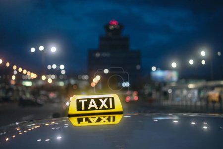 Photo for Selective focus on yellow taxi sign. Reflection in roof of car against airport terminal building at night. - Royalty Free Image