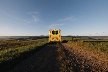 Photo for Ambulance car of emergency medical service leaving on rural dirt road in the middle of fields. Themes urgency, rescue and health care in remote location - Royalty Free Image
