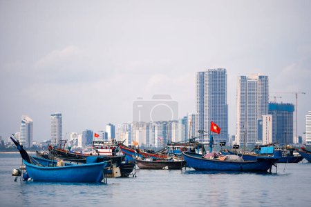 Foto de Enfoque selectivo en bandera vietnamita en barco pesquero amarrado en puerto contra costa con edificios modernos. Paisaje urbano de Da Nang en Vietnam - Imagen libre de derechos