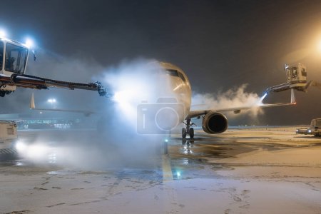 Photo for Deicing of airplane before flight. Winter frosty night and ground service at airport during snowfall - Royalty Free Image