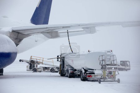 Photo for Refueling of airplane from fuel tanker truck at airport during snowfall. Ground service before flight on frosty winter day. - Royalty Free Image