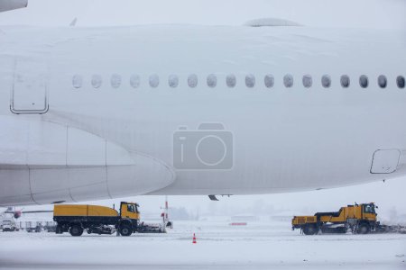 Foto de Día helado de invierno en el aeropuerto durante las fuertes nevadas. Avión cubierto de nieve contra quitanieves despejando pista del aeropuerto - Imagen libre de derechos