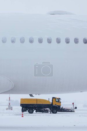 Foto de Día helado de invierno en el aeropuerto durante las fuertes nevadas. Avión cubierto de nieve contra quitanieves despejando pista del aeropuerto - Imagen libre de derechos