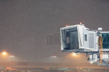 Téléchargez les photos : Hiver nuit givrée à l'aéroport lors de fortes chutes de neige. Élimination du pont d'embarquement vide des passagers contre le ciel sombre avec des flocons de neige. - en image libre de droit