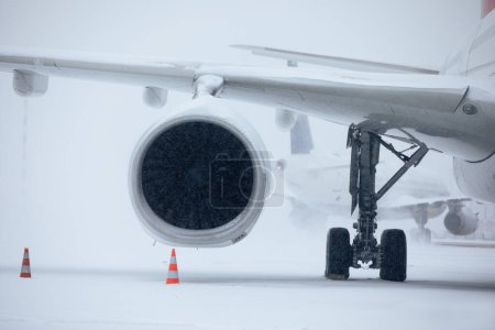 Photo for Traffic at airport during heavy snowfall. Snowflakes against jet engine and taxiing airplane at airport taxiway during frosty winter day. Extreme weather in transportation - Royalty Free Image