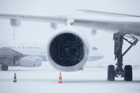 Foto de Tráfico en el aeropuerto durante las fuertes nevadas. Copos de nieve contra el motor a reacción y el avión rodante en la pista de rodaje del aeropuerto durante el helado día de invierno. Clima extremo en el transporte - Imagen libre de derechos