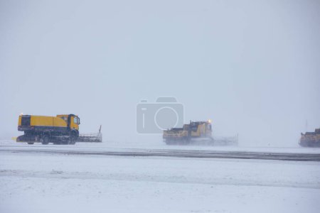 Photo for Closed airport during heavy snowfall. Snow plows removing snow from closed runway. Contept of extreme weather in transportation with copy space. - Royalty Free Image