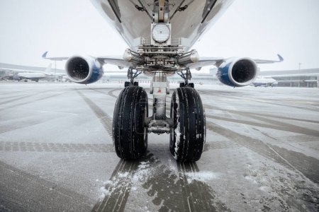 Téléchargez les photos : Vue de face du train d'atterrissage de l'avion. Journée givrée d'hiver à l'aéroport pendant les chutes de neige. - en image libre de droit