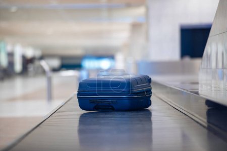 Foto de Viajando en avión. Enfoque selectivo en la maleta azul solitaria en la recogida de equipaje en la terminal del aeropuerto - Imagen libre de derechos
