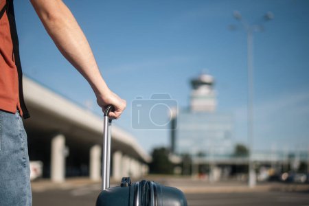 Téléchargez les photos : Voyage en avion. Le voyageur se rend à pied du parking au terminal de l'aéroport. Homme avec valise contre tour de contrôle de la circulation aérienne le jour ensoleillé de l'été. - en image libre de droit