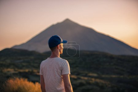 Téléchargez les photos : Vue arrière homme regardant le paysage avec le volcan Teide au coucher du soleil. Touriste lors d'une randonnée sur l'île canarienne de Tenerife - en image libre de droit