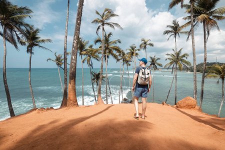 Photo for Traveler with backpack walking among coconut palm trees on hill aagainst tropical beach in Sri Lanka. - Royalty Free Image