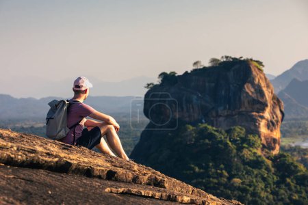 Photo for Man with backpack sitting on rock and looking at landscape. Scenery with Sigiriya rock in Sri Lanka. - Royalty Free Image