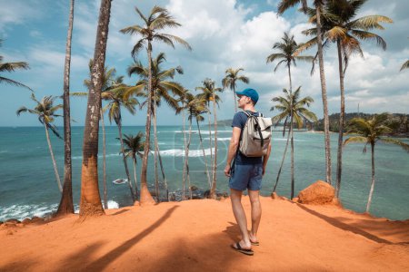 Photo for Traveler with backpack walking among coconut palm trees on hill aagainst tropical beach in Sri Lanka. - Royalty Free Image
