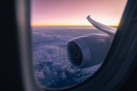 Téléchargez les photos : Belle vue depuis la fenêtre de l'avion sur le moteur à réaction et l'aile. Avion volant au-dessus des nuages au crépuscule Thèmes aviation, voyage et connexion - en image libre de droit