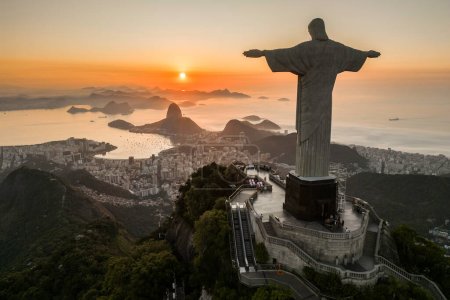 Photo for Rio de Janeiro, Brazil - March 21, 2023: Christ the Redeemer statue on top of the Corcovado Mountain with the Sugarloaf Mountain in the  horizon on sunrise. - Royalty Free Image
