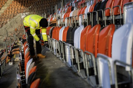 Téléchargez les photos : Un ouvrier visse une vis tout en remplaçant les sièges au stade - en image libre de droit