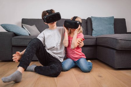 Foto de Niños asombrados usando gafas de realidad virtual jugando juegos en la sala de estar en casa. Hermano y hermana - Imagen libre de derechos