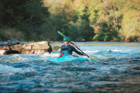 Foto de Joven adolescente navegando por rápidos de aguas bravas en un kayak azul, hermosa naturaleza fluvial en un día soleado de verano, toma de mano. - Imagen libre de derechos