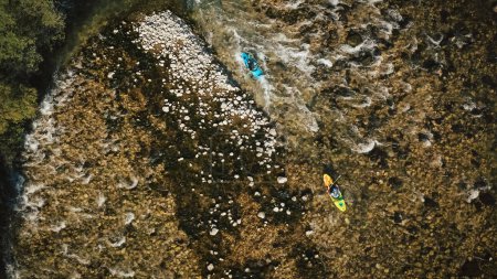 Téléchargez les photos : Deux athlètes récréatifs faisant du kayak sur de l'eau en mouvement rapide, pagayant et manœuvrant avec succès entre les obstacles rocheux de la rivière, vue aérienne sur un drone. - en image libre de droit