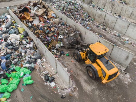 Foto de Handling construction waste on the landfill site, skid steer loader scooping and dumping dusty trash, aerial side view. - Imagen libre de derechos