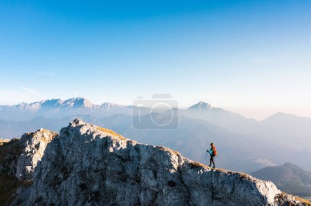 Photo for Mountaineering on the mountain, a young woman hiking on the trail with trekking poles on the top of the ridge - Royalty Free Image