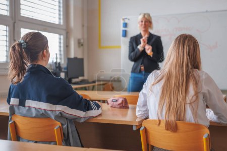 Téléchargez les photos : Vue arrière de deux étudiantes lors d'une conférence en classe, regardant l'enseignement et l'écriture des enseignantes sur un tableau noir - en image libre de droit