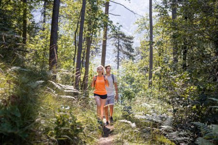 Lächelndes junges Paar mit Rucksack, Freizeitwanderer genießen Wanderungen durch einen grünen Wald, wandern bergauf.