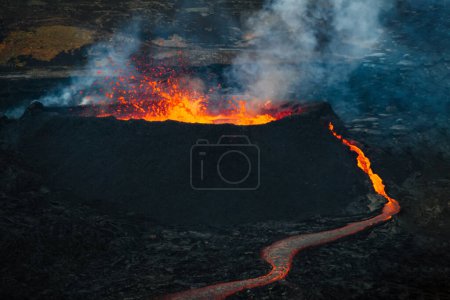 Vulkanausbruch in Island, eine Fontäne glühend roter Lava steigt über einen Schlot und ein Lavastrom breitet sich rasch bergab aus, Luftaufnahme.
