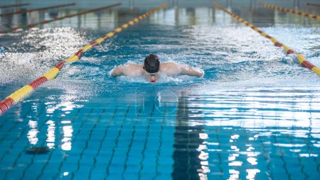 Photo for Male professional athlete swimming in butterfly style, with both arms moving symmetrically, making water splash - Royalty Free Image