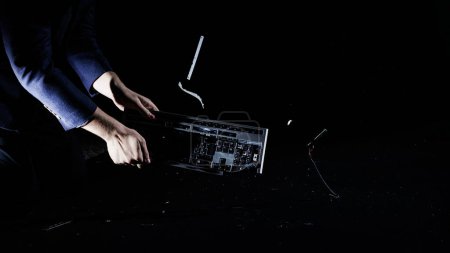 Mann schlägt und schlägt Computertastatur auf hartem Boden, isoliert auf schwarzem Hintergrund, Zeitlupenaufnahme. Arbeitsplatzangst, Burnout der Mitarbeiter und moderne Lebensstilkonzepte.