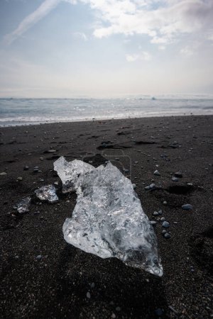 Des vagues océaniques tapissent des morceaux de glace scintillant au soleil sur une plage de sable noir. Merveille naturelle, Islande, glaciers et icebergs concepts.