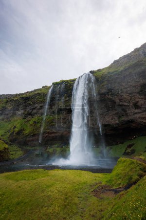 Téléchargez les photos : Seljalandsfoss, une cascade célèbre et unique en Islande avec des visiteurs marchant derrière les chutes dans une petite grotte. Concept de voyage. - en image libre de droit