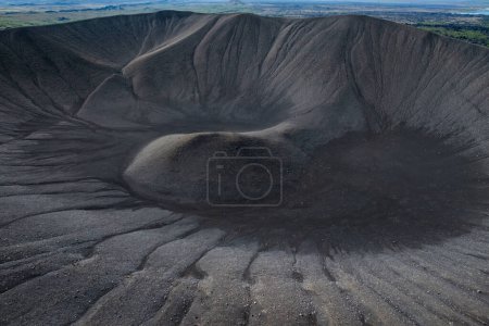 Majestic view of an erupted volcano crater with black sand and scenic landscape in the background, aerial shot. Nature wonder concept.