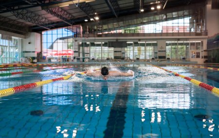Profesional nadador masculino realizando estilo mariposa en el carril de la piscina de regazo interior, vista frontal. Concepto de éxito, motivación y esfuerzo.
